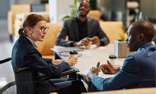 Side view portrait of successful businesswoman using wheelchair at meeting and talking to group of colleagues in modern office space