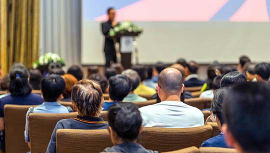 Back side of audience listening the Speaker with podium on the stage in the conference hall