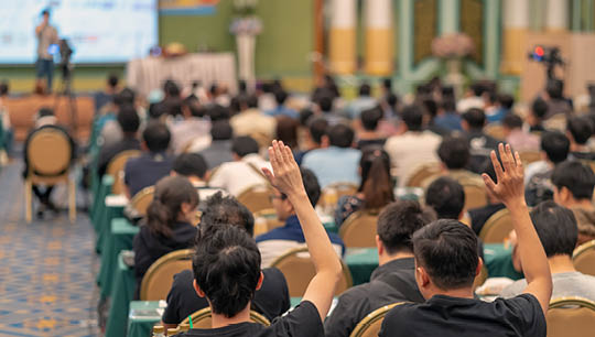 Rear view of Audience showing hand to answer the question from Speaker on the stage