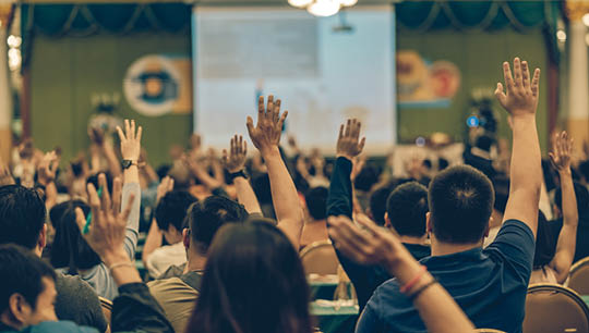 Rear view of Audience showing hand to answer the question from Speaker on the stage